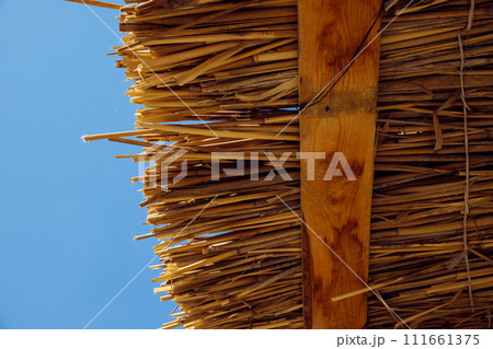 dry reed roof texture, thatched roof, palapa roof in blue sky. Wooden beach sun summer canopy. View from below dry reed roof texture, thatched roof, palapa roof in blue sky. Wooden beach sun summer canopy. View from below 111661375