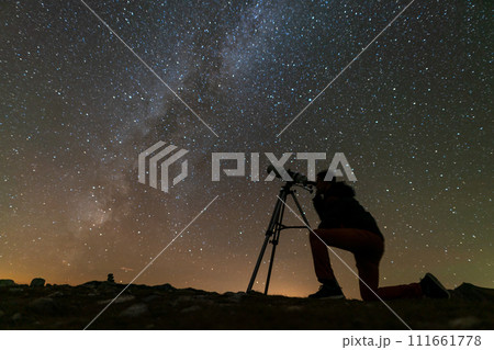 a man looks through a telescope on a tripod at the starry sky 111661778