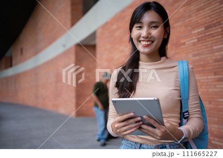 Young and cute Asian college student girls smile carrying a backpack with a textbooks in front of the university campus building. learning materials, importance of education becoming intelligent 111665227