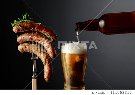 Beer and grilled Bavarian sausages with rosemary. Sausages on a fork sprinkled with rosemary. 111668819