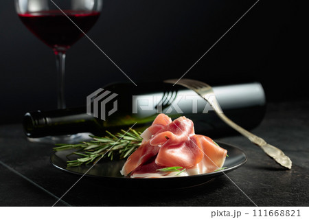 Prosciutto with rosemary and red wine on a black background. Prosciutto with rosemary and red wine on a black background. 111668821