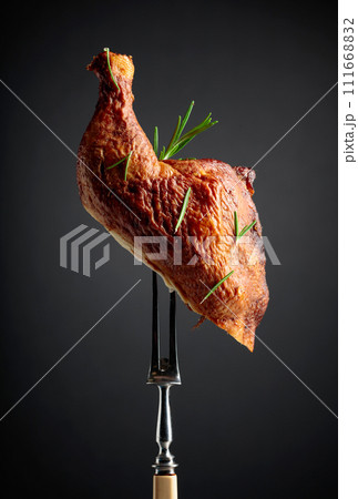 Smoked chicken thigh on a fork sprinkled with rosemary. 111668832