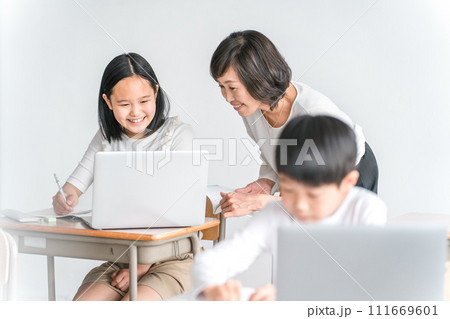 学校の教室でノートパソコンを使いながら勉強する女子小学生と女性講師（教育・先生・授業・家庭教師） 111669601
