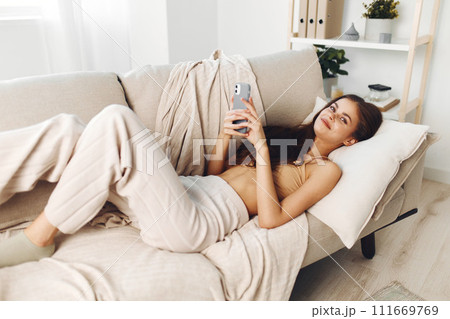 Smiling Woman Holding Mobile Phone on Cozy Sofa in Living Room Smiling Woman Holding Mobile Phone on Cozy Sofa in Living Room 111669769