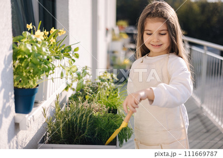 Cute little girl starting for landing on balcony. Side view of four year old girl use small shovel for soil 111669787