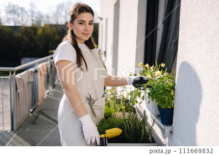 Attractive woman start landing on balcony. Young female in light striped overalls planting 111669832
