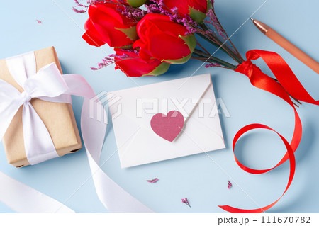 White envelope with heart, kraft gift box and rose on blue background 111670782