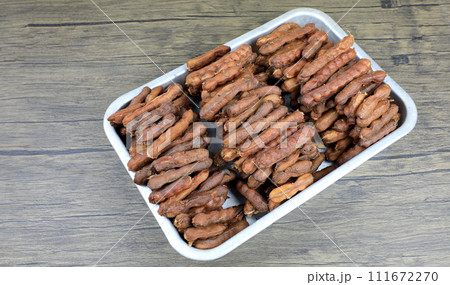 Tropical tamarind fruit without a shell, with visible seeds and inner pulp, in a galvanized tray on a wooden. Concept of food preservation in Thai style. Peeled tamarind is a ready-to-eat concept. 111672270