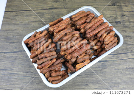Tropical tamarind fruit without a shell, with visible seeds and inner pulp, in a galvanized tray on a wooden. Concept of food preservation in Thai style. Peeled tamarind is a ready-to-eat concept. 111672271