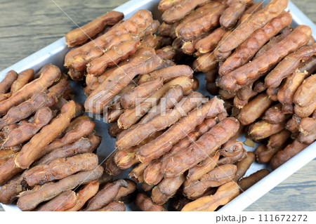 Tropical tamarind fruit without a shell, with visible seeds and inner pulp, in a galvanized tray on a wooden. Concept of food preservation in Thai style. Peeled tamarind is a ready-to-eat concept. 111672272