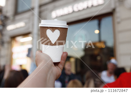 paper cup of coffee with carved white heart in women's hand on center of city - Nevsky Prospekt in St. Petersburg 111672847