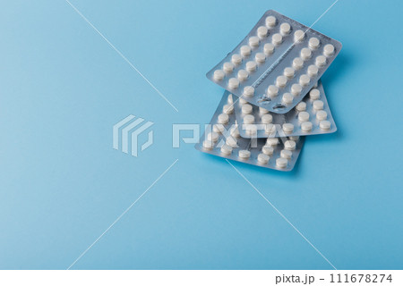 Medical background of many white capsule tablets or pills on blue table Medical background of many white capsule tablets or pills on blue table 111678274