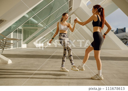 Happy female friends doing gesture of sport shake hand and legs after exercising outside 111678613