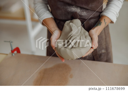 Close up of woman preparing clay to create a mug on a wooden table in pottery studio Close up of woman preparing clay to create a mug on a wooden table in pottery studio 111678699