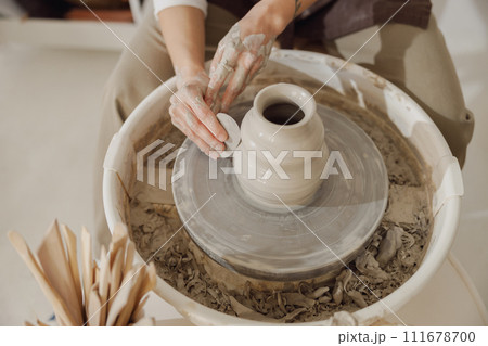 Female potter in apron making shape of clay vase on spinning pottery tool in ceramic workshop 111678700