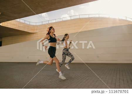 Young women in sportswear are running on modern buildings background. Active lifestyle concept Young women in sportswear are running on modern buildings background. Active lifestyle concept 111678701
