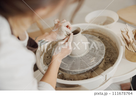 Female potter in apron making shape of clay vase on spinning pottery tool in ceramic workshop Female potter in apron making shape of clay vase on spinning pottery tool in ceramic workshop 111678764