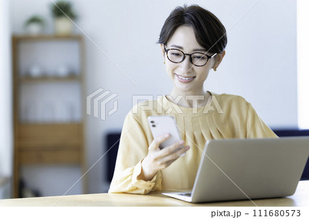 ノートパソコンを使いながらスマホを操作するミドル女性 111680573