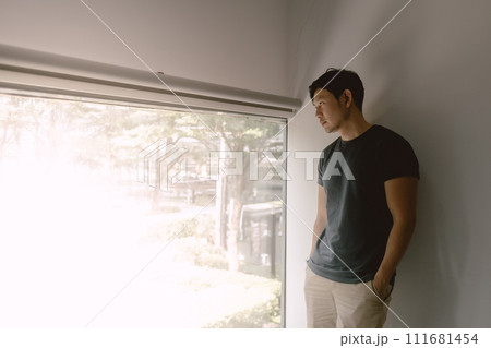 Asian man leaning against a wall, gazes out the window Asian man leaning against a wall, gazes out the window 111681454