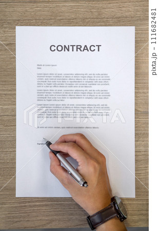 Closeup man hand holding a pen signing his name on a CONTRACT document. Top View 111682481