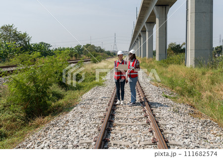 Two people are standing on railroad tracks and looking at laptop computer together. 111682574