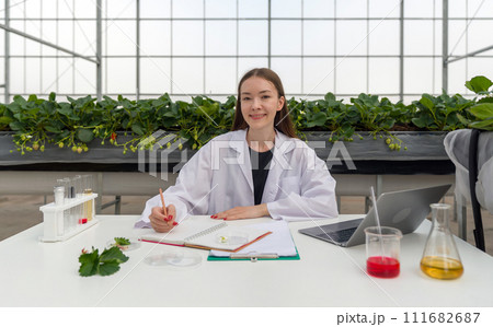 A scientist conducting research with a laptop within a vegetation-rich greenhouse. A scientist conducting research with a laptop within a vegetation-rich greenhouse. 111682687