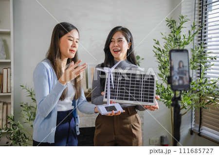 Two female salespeople are live-streaming a sale on their mobile phones Two female salespeople are live-streaming a sale on their mobile phones 111685727