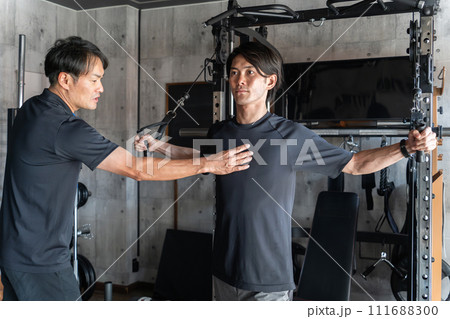 パーソナルジムでトレーナーに指導・レッスンを受ける若いアジア人男性（ケーブルフライ・パワーラック） 111688300