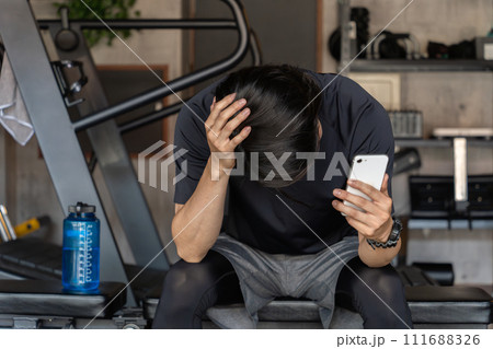 ジム・トレーニングジムで頭を抱えて悩む・落ち込むアジア人男性（廃業・失敗・怪我・炎上） 111688326