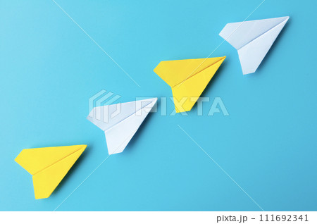 Top view of white and yellow paper airplanes origami flying on blue background Top view of white and yellow paper airplanes origami flying on blue background 111692341