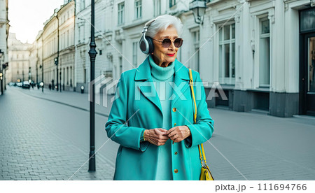 An older woman in casual stylish clothes listens to music on headphones. Active aging, walk around the city An older woman in casual stylish clothes listens to music on headphones. Active aging, walk around the city 111694766