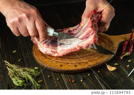 The chef cuts raw ribs with a knife on a wooden board. The concept of the process of preparing a meat dish. Asian cuisine 111694793