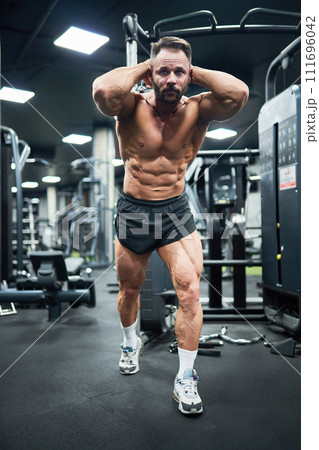Focused bearded bodybuilder with strong abs, pulling weight, training in gym. Low angle view of handsome determined guy with hands behind head, exercising, working out indoor. Concept of bodybuilding. Focused bearded bodybuilder with strong abs, pulling weight, training in gym. Low angle view of handsome determined guy with hands behind head, exercising, working out indoor. Concept of bodybuilding. 111696042