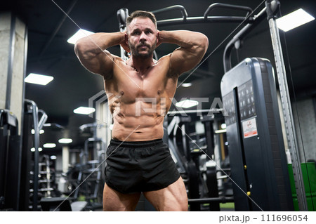 Determined dark-haired man with strong abs, pulling weights, training in gym. Low angle view of handsome Caucasian guy exercising, working out at evening. Concept of bodybuilding, crossfit, sport.  111696054