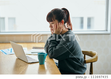パソコンを見ながら頬杖をついて考え事をする若い女性 パソコンを見ながら頬杖をついて考え事をする若い女性 111697435