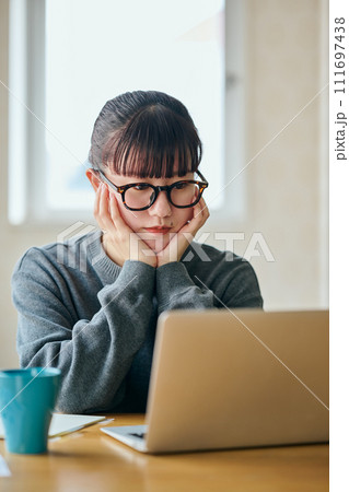 パソコンを見ながら頬杖をついて考え事をする若い女性 111697438