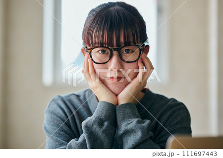 頬杖をついて考え事をするカメラ目線の若い女性 頬杖をついて考え事をするカメラ目線の若い女性 111697443