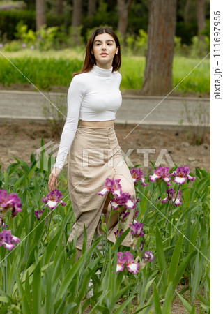Side view of attractive, slim, brunette female walking in flowers in garden, looking aside, enjoying. Concept of springtime. 111697986
