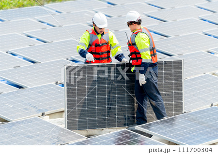 Two Asian professional technician workers with safety uniform stand and help to check or maintenance solar cell panels in area of workplace over water reservoir. 111700304