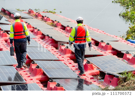 Back and side view of professional with safety uniform walk on footpath along row of solar cell panels in workplace concept of green energy power plant for good environment. 111700372