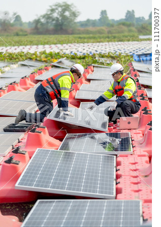 Vertical image of professional technician worker use laptop to work with other co-worker touch to check and maintenance solar cell panel in workplace over water reservoir. Vertical image of professional technician worker use laptop to work with other co-worker touch to check and maintenance solar cell panel in workplace over water reservoir. 111700377