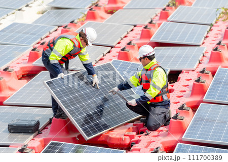 Close up two technician workers help to check and maintenance solar cell panels that set up over area of water reservoir. Close up two technician workers help to check and maintenance solar cell panels that set up over area of water reservoir. 111700389