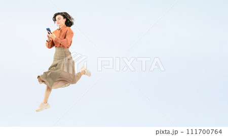 スマホを見ながらジャンプする白人女性の全身写真 111700764