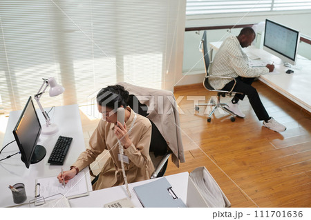 Office manager filling document with clients data when working at her desk 111701636