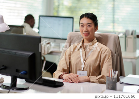 Portrait of smiling businesswoman checking text messages on smartphone when working at office desk 111701660