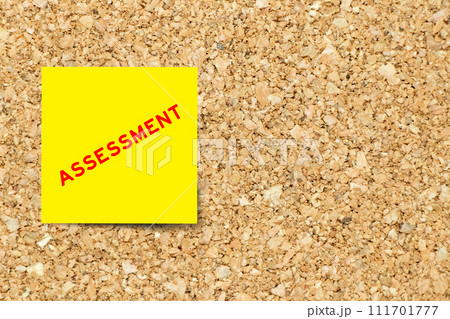 Yellow note paper with word assessment on cork board background with copy space Yellow note paper with word assessment on cork board background with copy space 111701777