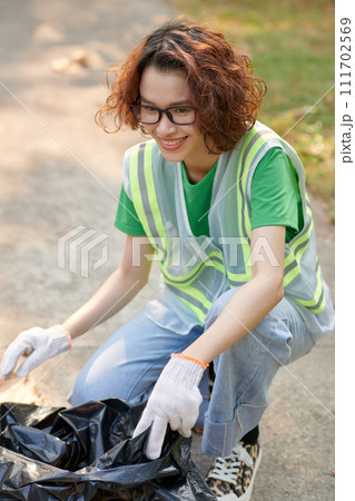 Cheerful Vietnamese girl wearing textile gloves when collecting garbage in park Cheerful Vietnamese girl wearing textile gloves when collecting garbage in park 111702569
