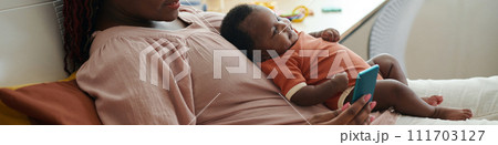 Web banner with mother sitting on bed with baby and texting friends Web banner with mother sitting on bed with baby and texting friends 111703127