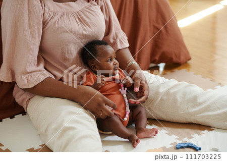 Mother sitting on floor with baby girl between her legs when playing together Mother sitting on floor with baby girl between her legs when playing together 111703225