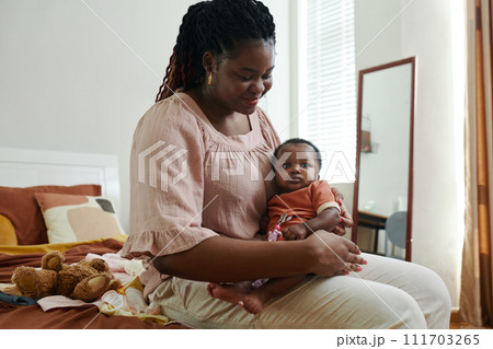 Smiling Black woman sitting on bed with baby girl on her laps 111703265
